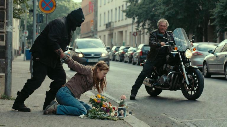 DER SCHLÄGER IN DRESDEN STIEẞ DIE JUNGE FRAU ZU BODEN, ALS SIE AM STRAẞENRAND BLUMEN FÜR IHREN VATER NIEDERLEGTE. EIN ALTER BIKER HIELT AN, SAH DAS FOTO DES VATERS AUF DEM BLUMENSTRAUẞ UND ERSTARRTE. ES WAR SEIN ALTER KAMERAD, DER EINST SEIN LEBEN GEGEBEN HATTE, UM DIE GANZE BIKERGRUPPE ZU RETTEN. DER SCHLÄGER WURDE AM KRAGEN GEPACKT UND AUF DEN ASPHALT GEDRÜCKT, WÄHREND ER ZITTERTE UND ES NICHT WAGTE, DEN KOPF ZU HEBEN.